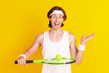 Portrait of attractive skilled cheerful guy playing tennis holding ball on racket isolated over bright yellow color background