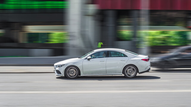 Side view rolling shot with white car in motion. Mercedes CLA Class driving along the street in city with blurred background