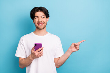 Photo of cunning millennial brunet guy hold telephone look empty space wear white t-shirt isolated...