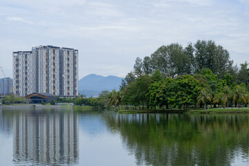 Fototapeta na wymiar peaceful scene of cityscape in Kepong, Kuala Lumpur, Malaysia. Greenery woods, high-rise buildings, hills and clear cloud sky in background with reflection on water. 
