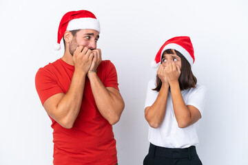 Young couple with christmas hat isolated on white background is a little bit nervous and scared putting hands to mouth