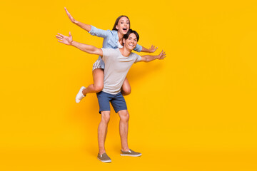 Full length body size view of attractive cheery couple piggy backing summertime jet isolated vivid yellow color background