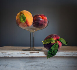 Ripe peaches in a glass vase and another on the table.