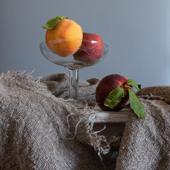 Ripe peaches in a glass vase and another on the table.