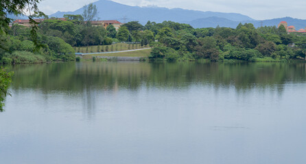 Beautiful and peaceful view of a lake in the outskirt of Kepong, Kuala Lumpur, Malaysia. Still water, reflection of green trees being the main focus, hills and clear cloud sky in background. 