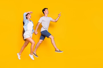 Fototapeta na wymiar Full length body size view of handsome beautiful trendy couple jumping running showing copy space isolated vivid yellow color background