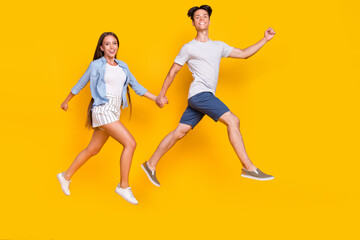 Fototapeta na wymiar Full length body size view of handsome beautiful trendy couple jumping running active isolated over vivid yellow color background