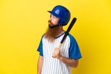 Redhead baseball player man with helmet and bat isolated on yellow background looking to the side