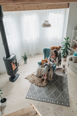 Remote work. Young woman using laptop in a cozy armchair and plaid sitting by the fireplace with a...