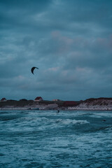 A active and sporty kitesurfer on the north sea beach with colorful sunset colors and wild windy ocean with sunset vibes. Dramatic stormy with a surfer jumping and having fun. Lokken, Denmark
