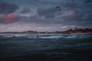 A active and sporty kitesurfer on the north sea beach with colorful sunset colors and wild windy ocean with sunset vibes. Dramatic stormy with a surfer jumping and having fun. Lokken, Denmark