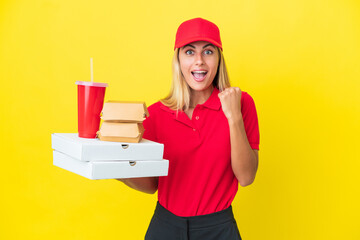 Delivery Uruguayan woman holding fast food isolated on yellow background celebrating a victory in winner position