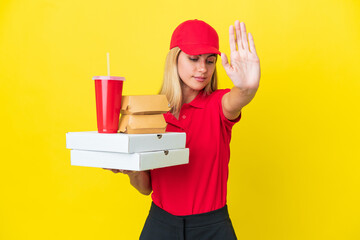 Delivery Uruguayan woman holding fast food isolated on yellow background making stop gesture and disappointed