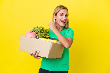 Young Uruguayan girl making a move while picking up a box full of things isolated on yellow background celebrating a victory