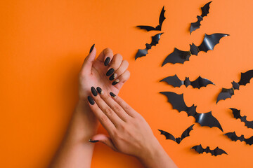 Halloween Nail Art Design. Flat lay with bats and beautiful manicure on hands on orange background