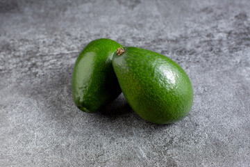 two green avocados lie on an artificial stone board. diet food. green vegetable.