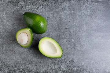 two green avocados lie on an artificial stone board. diet food. green vegetable.avocado cutaway....