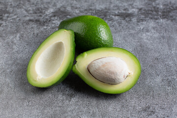 two green avocados lie on an artificial stone board. diet food. green vegetable.avocado cutaway. avocado seed.
