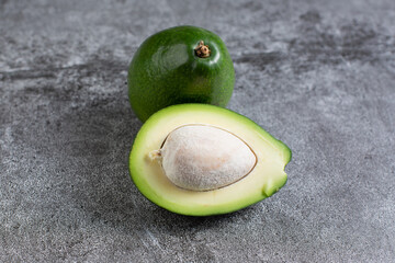 two green avocados lie on an artificial stone board. diet food. green vegetable.avocado cutaway. avocado seed.
