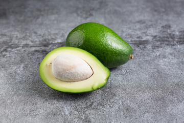 two green avocados lie on an artificial stone board. diet food. green vegetable.avocado cutaway. avocado seed.