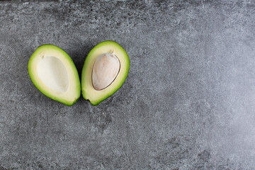 two green avocados lie on an artificial stone board. diet food. green vegetable.avocado cutaway. avocado seed. space for design and for text