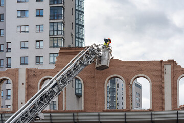 A worker in a construction cradle dismantles the facade of an old building