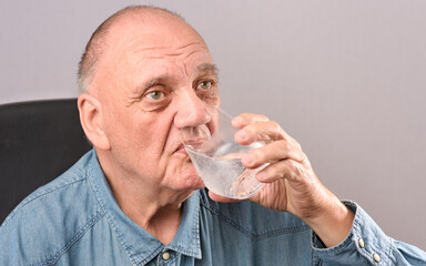Fototapeta na wymiar homme âgé boit un verre d'eau fraiche