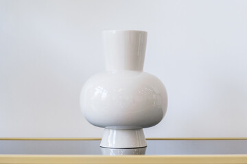 Fototapeta na wymiar White low ceramic vase against a white wall. Empty vase for room decoration. Minimalistic design of the premises. Modern interior details. Stylish room decoration.