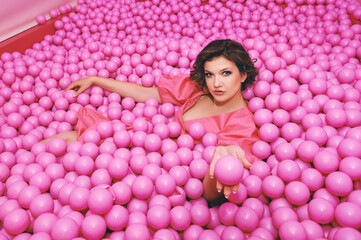 Obraz na płótnie Canvas Fashion portrait of happy young woman playing in a ball pit, wearing pink dress