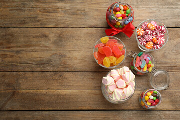 Jars with different delicious candies on wooden table, flat lay. Space for text