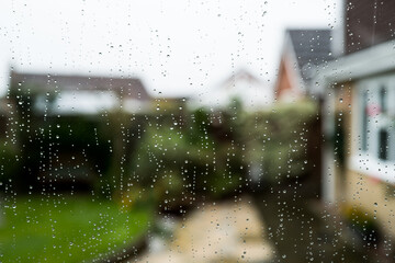 Shallow focus of rain droplets seen on a conservatory double glazed window looking out to a patio area. The weather has been particularly bad with heavy downpours. - obrazy, fototapety, plakaty