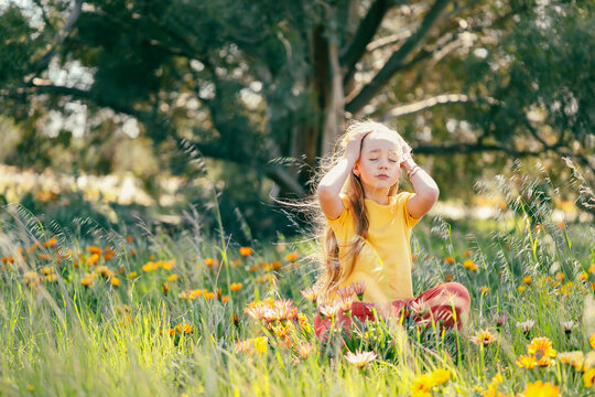 Portrait of pretty girl sitting in field with vibrant orange and yellow wildflowers