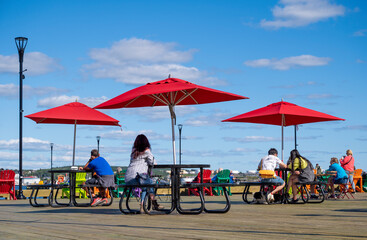 People sitting at tables with red umbrellas on the city embankment