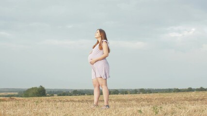 camera rotating around happy young pregnant woman in dress standing alone in field on background of cloudy rainy sky, relaxation on nature