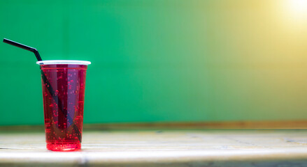 Red water in a plastic glass has a sucker tube, has a background and is sunny.