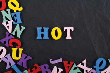 HOT word on black board background composed from colorful abc alphabet block wooden letters, copy space for ad text. Learning english concept.