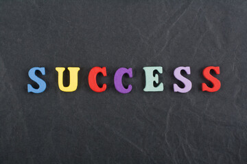 Obraz premium SUCCESS word on black board background composed from colorful abc alphabet block wooden letters, copy space for ad text. Learning english concept.