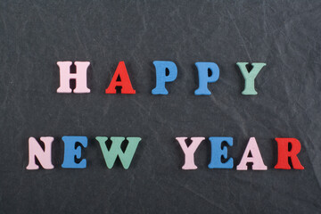 HAPPY NEW YEAR word on black board background composed from colorful abc alphabet block wooden letters, copy space for ad text. Learning english concept.