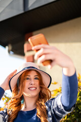 red-haired girl with a hat in the park takes a photo of herself in front of the building