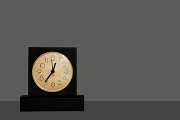 Black table clock with white dial standing on dark table