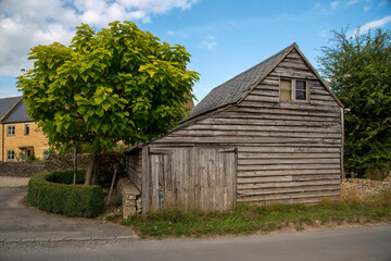 Fototapeta na wymiar Guiting Power, Gloucestershire, England, UK. 2021. An old wooden barn with small garage doors in the rural Cotswolds village of Guiting Power.