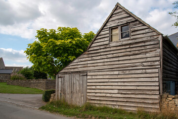 Fototapeta na wymiar Guiting Power, Gloucestershire, England, UK. 2021. An old wooden barn with small garage doors in the rural Cotswolds village of Guiting Power.