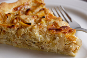 Close-up of a piece of onion tart, arranged on a white plate.