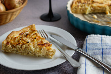 A piece of onion tart on a plate. Arranged on a gray concrete surface.