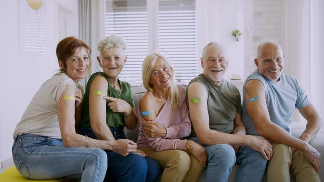 Group of senior friends showing plaster on arm indoors, covid-19 vaccination concept.