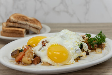 Loaded plate of skillet potatoes covered in two fired eggs, hot off the griddle served with toast