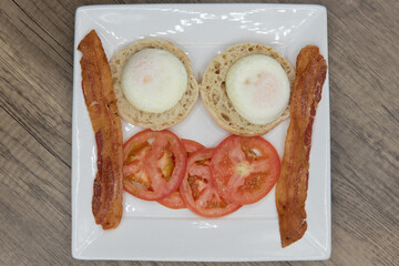 Overhead view of poached eggs sitting on english muffin served with bacon and sliced tomato for a hearty breakfast