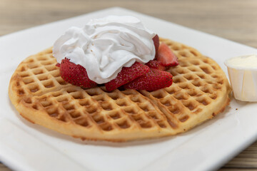 Hot waffle off the gridle topped with fresh chopped strawberries covered in whipped cream and served with butter on the side for a very hearty breakfast