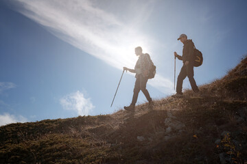 Two men silhouettes walking along the top of the mountain with backpacks hiking gear meets the...