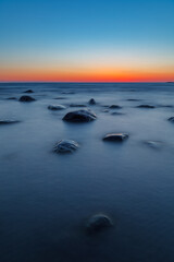 Fototapeta na wymiar Beautiful red strip of sunset over deep blue sea and boulders. Baltic sea, Estonia.